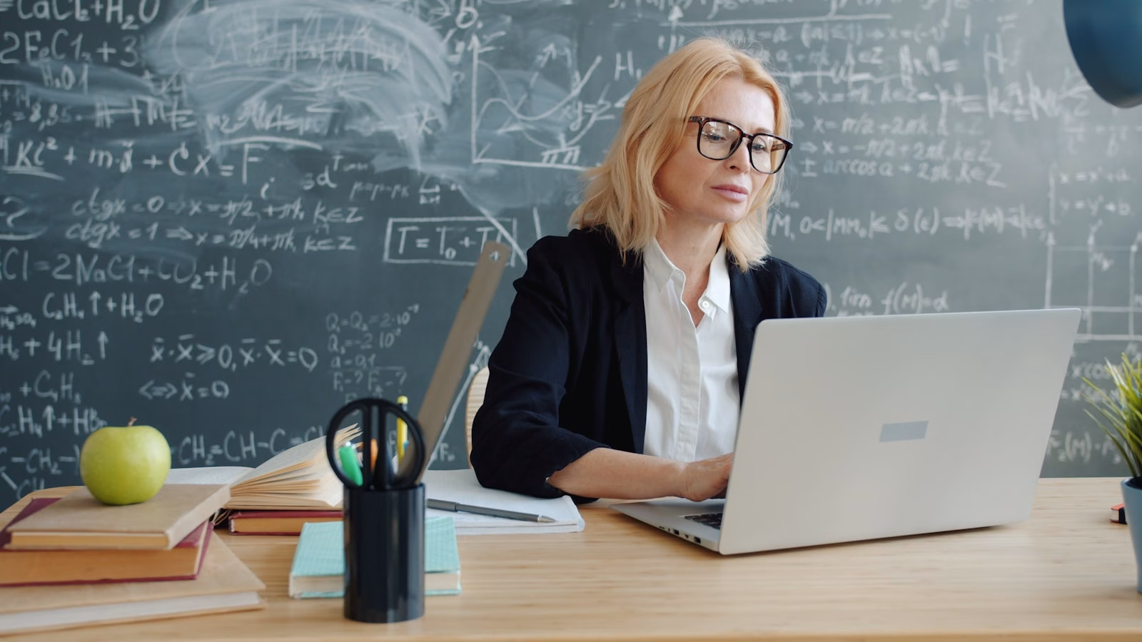 Teacher working on a laptop in front of a classroom board