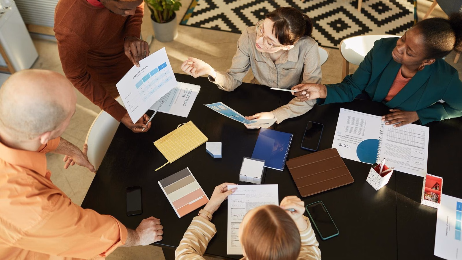 A diverse team discusses printed plans around a table during a workspace planning meeting.