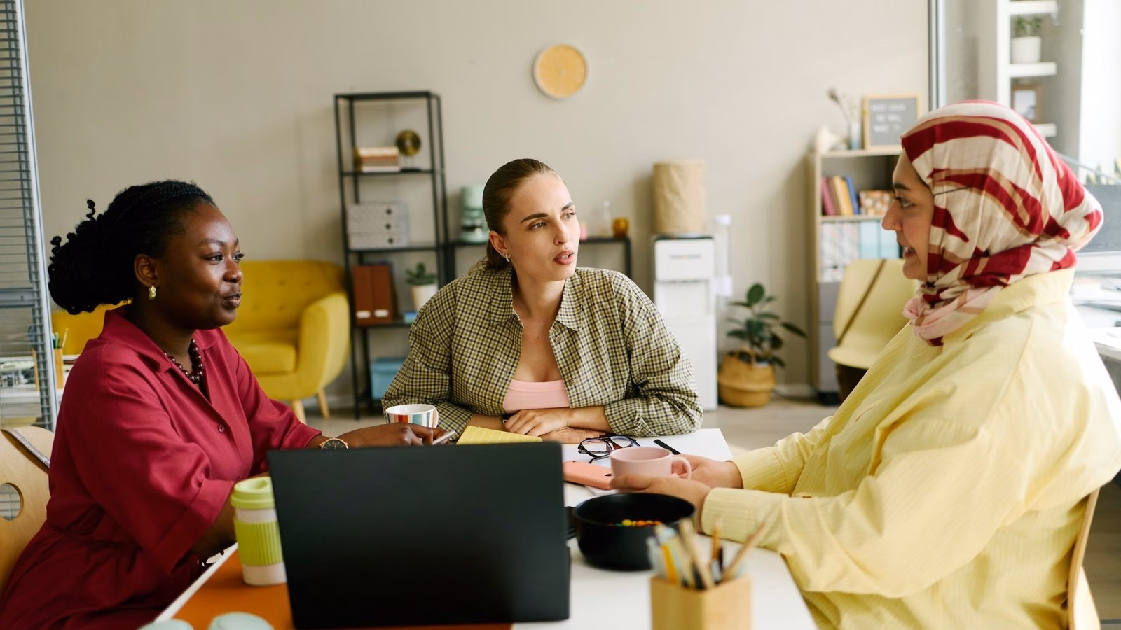 Three colleagues discuss a piece of work together around a laptop in an office.